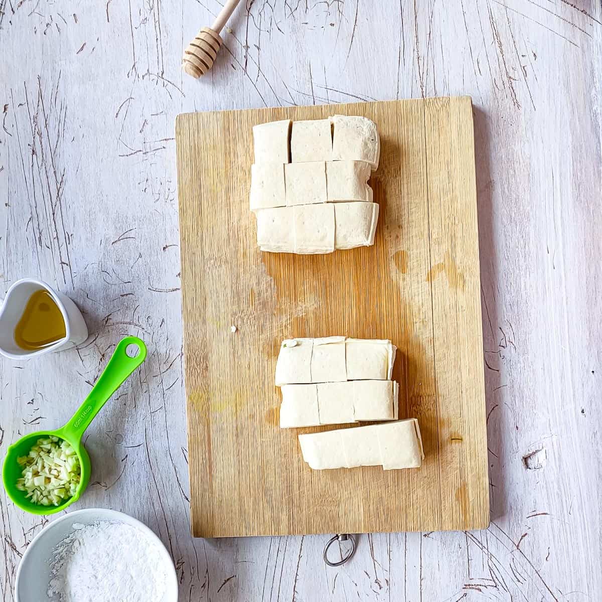 Horizotally sliced tofu blocks being sliced further into small pieces.