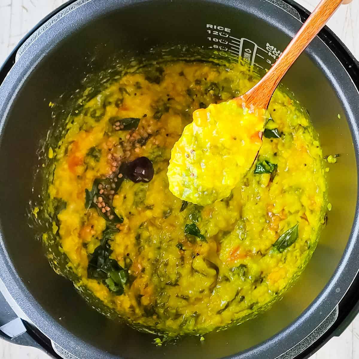 creamy moong dal palak in the instant pot with a ladle of dal scooped out.