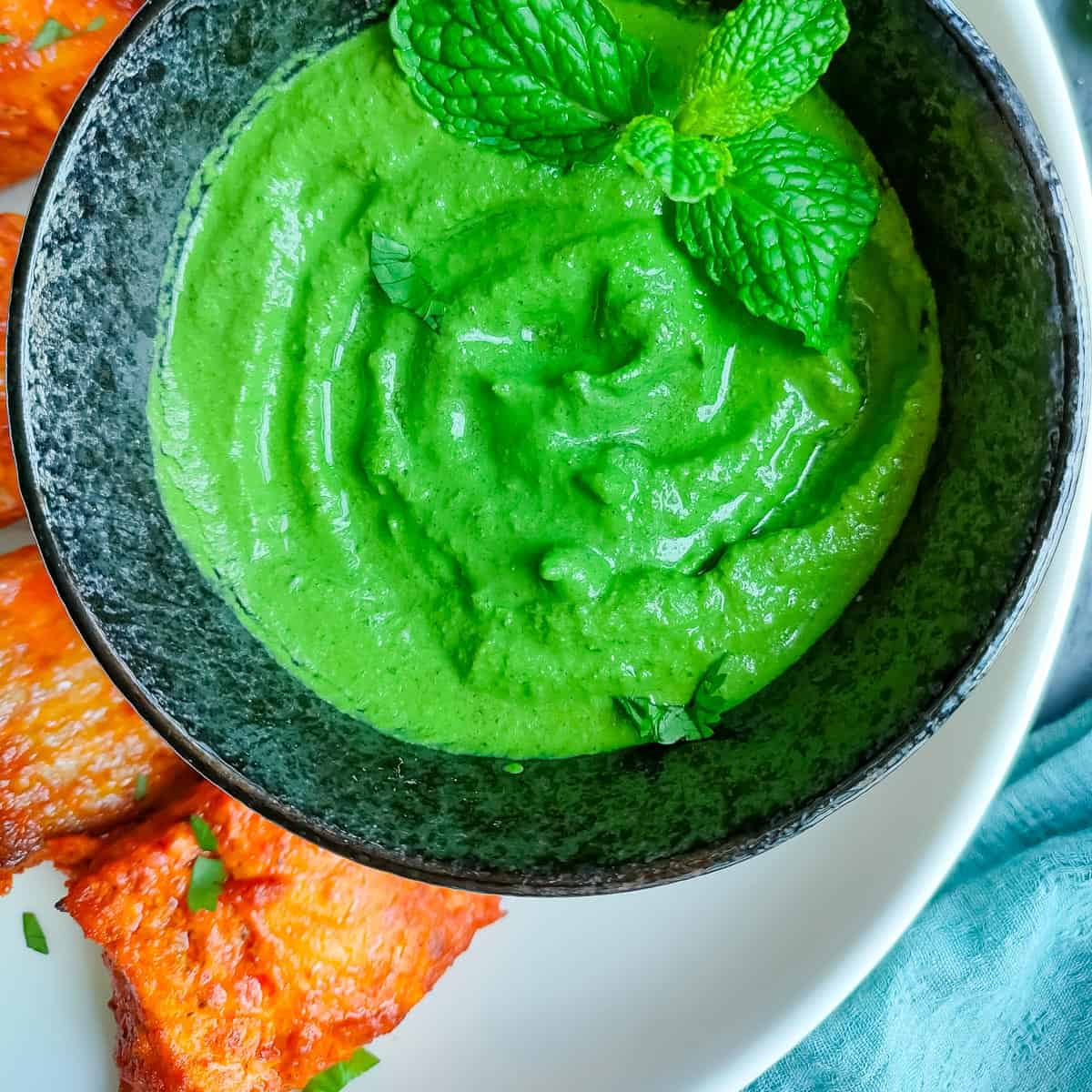 Restaurant style green chutney served in a black bowl with tandoori salmon on a white plate.