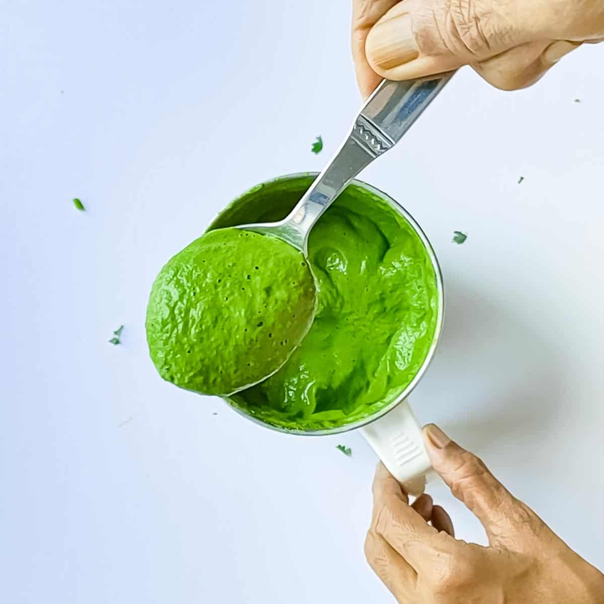 Green chutney for tandoori in a blender jar with a spoonful of chutney scooped out.