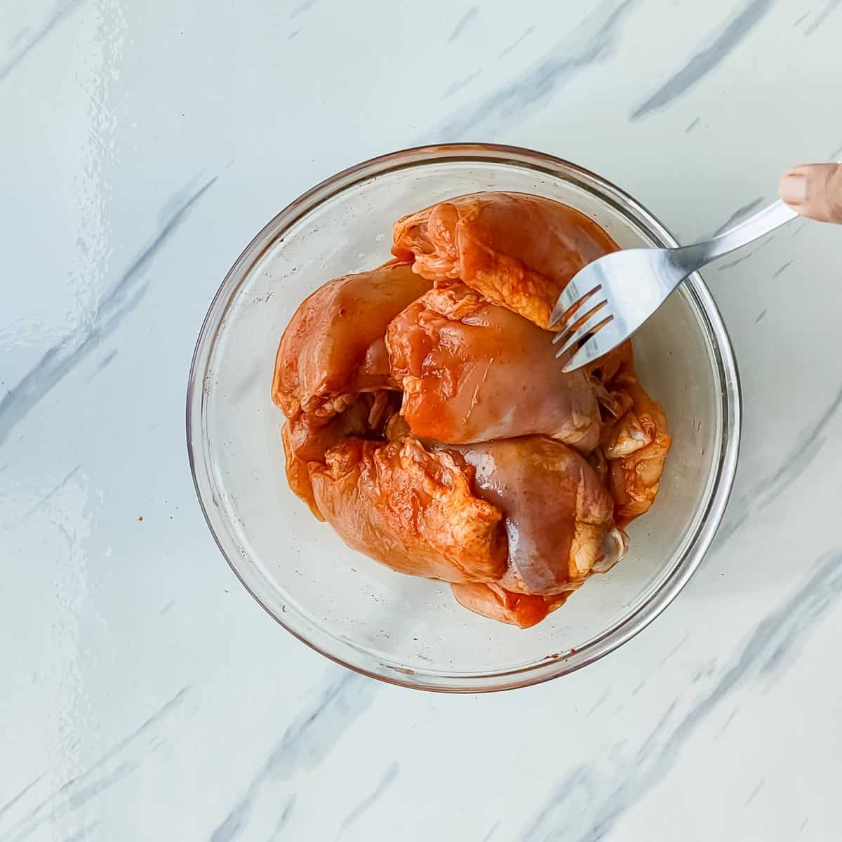 marinated chicken being pricked with a fork.