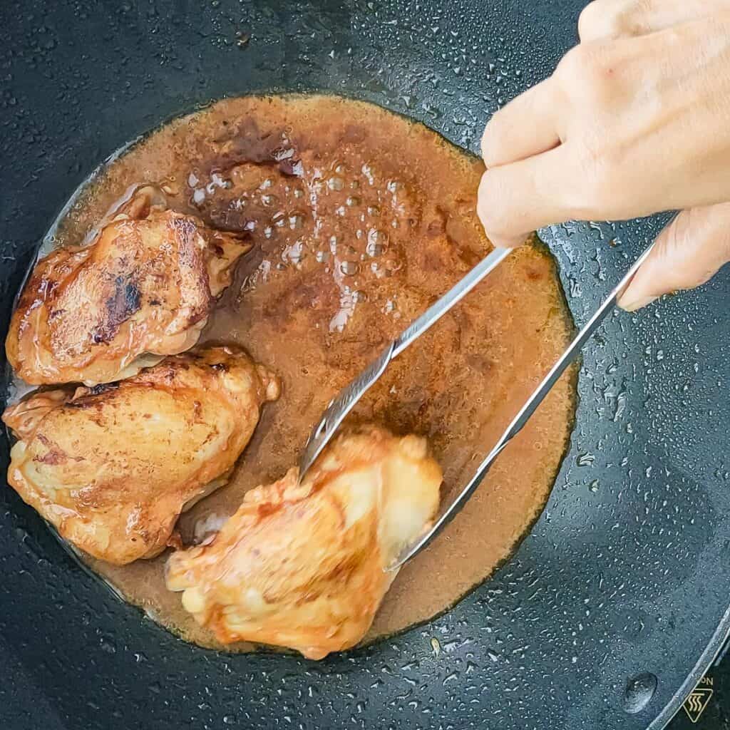 Browned chicken being added to simmering balsamic mustard sauce in a pan.