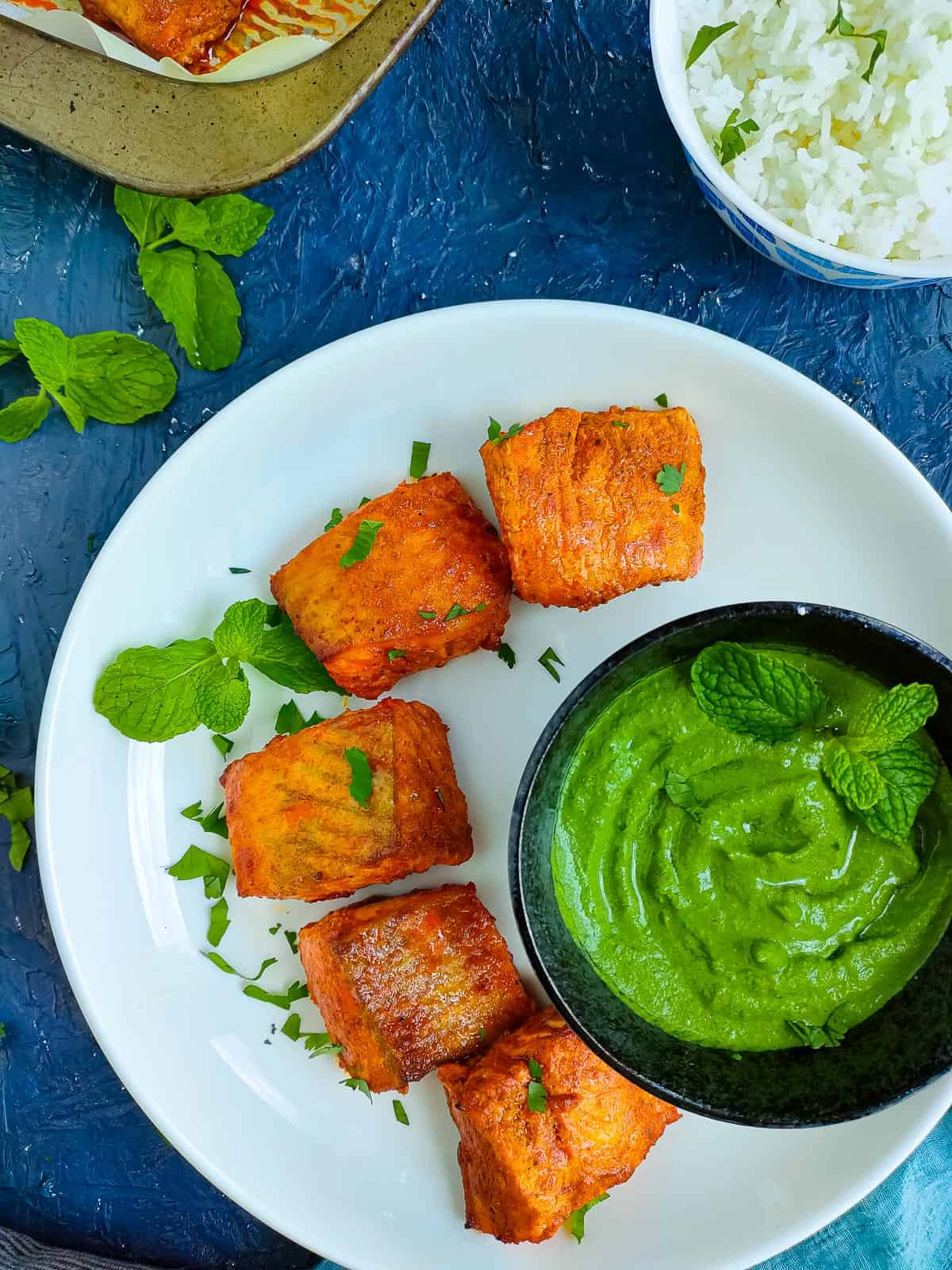 Salmon tandoori on a white plate served with a bowl of mint sauce.