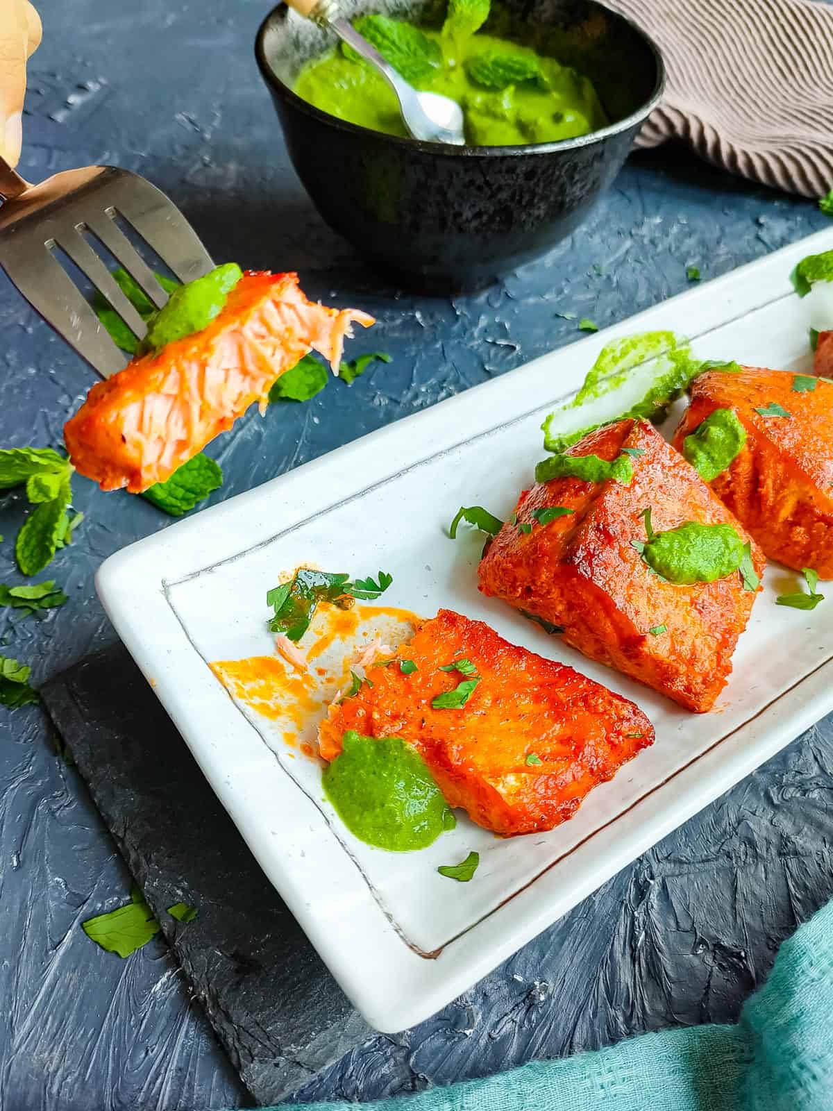 Salmon tandoori pieces with mint sauce and a fork with a piece of salmon.