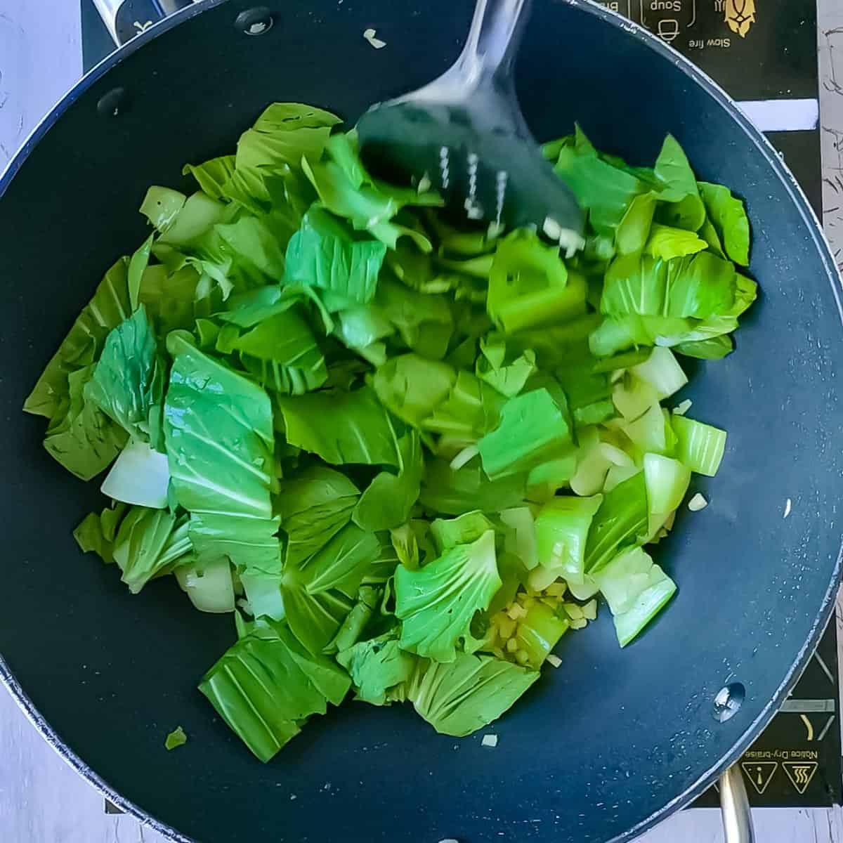 Bok choy leaves being stir fried in a pan.