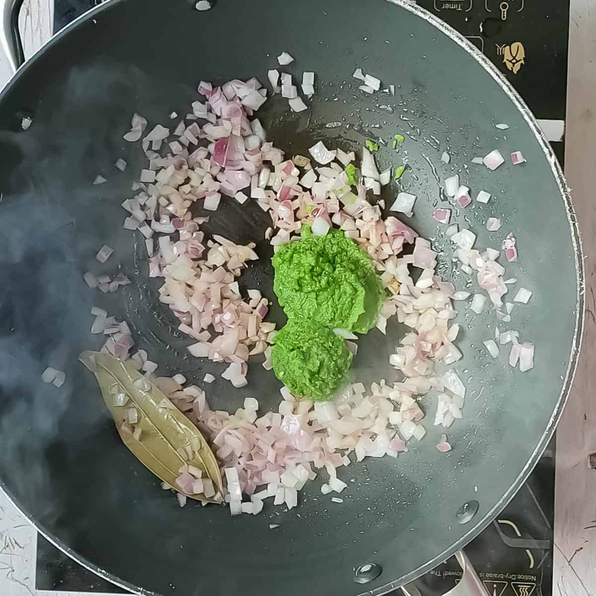 Green paste being added to sauteed onions in a non-stick pan.