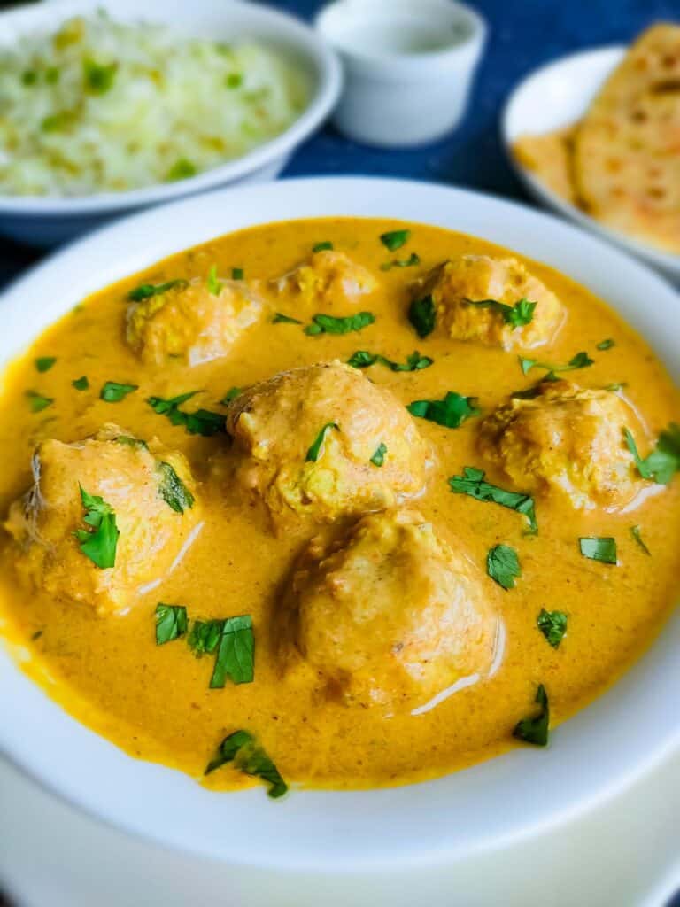 Chicken kofta curry in a white bowl and rice and rotis in the background.