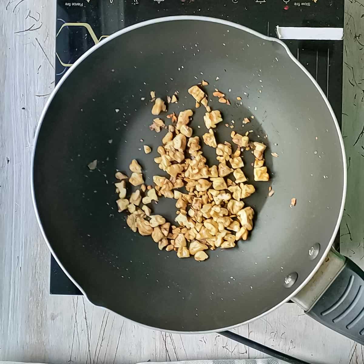 Walnuts being toasted in a pan for Thai basil pesto.