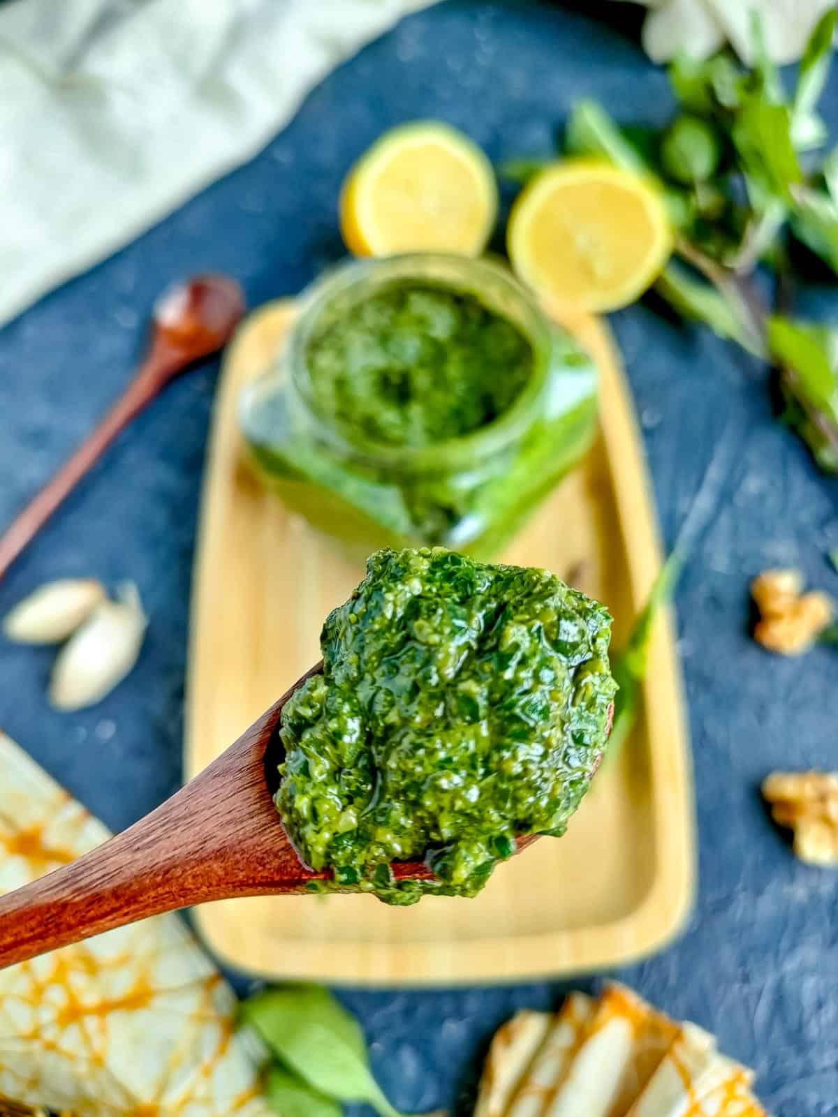 Thai basil pesto in a wooden spoon with a jar of pesto in the background.