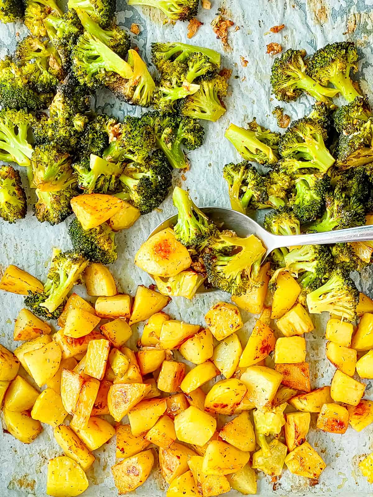 Oven-roasted potatoes and broccoli on a sheet pan with a spoon in it.