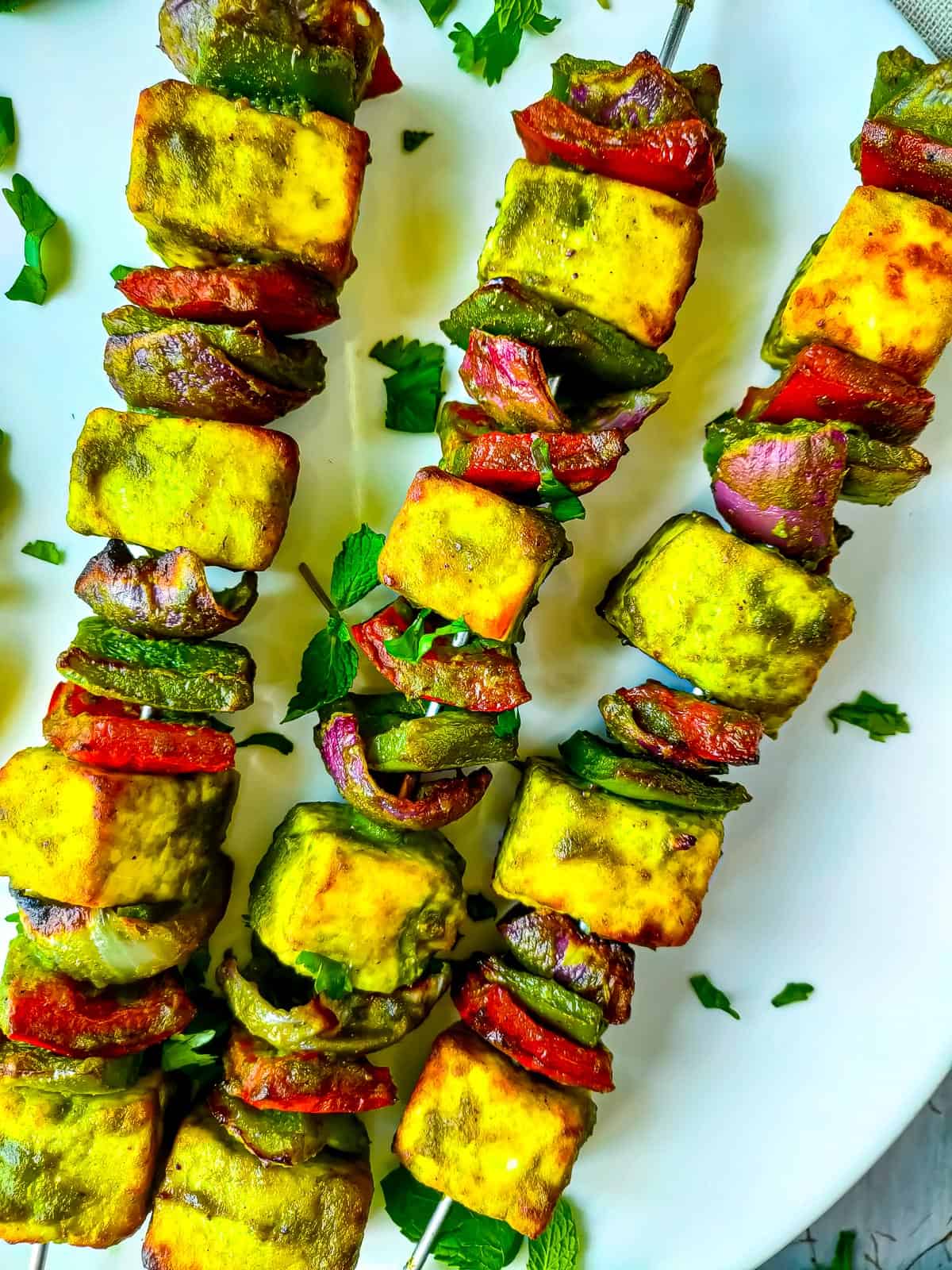 Hariyali paneer tikka on skewers served on a white plate.