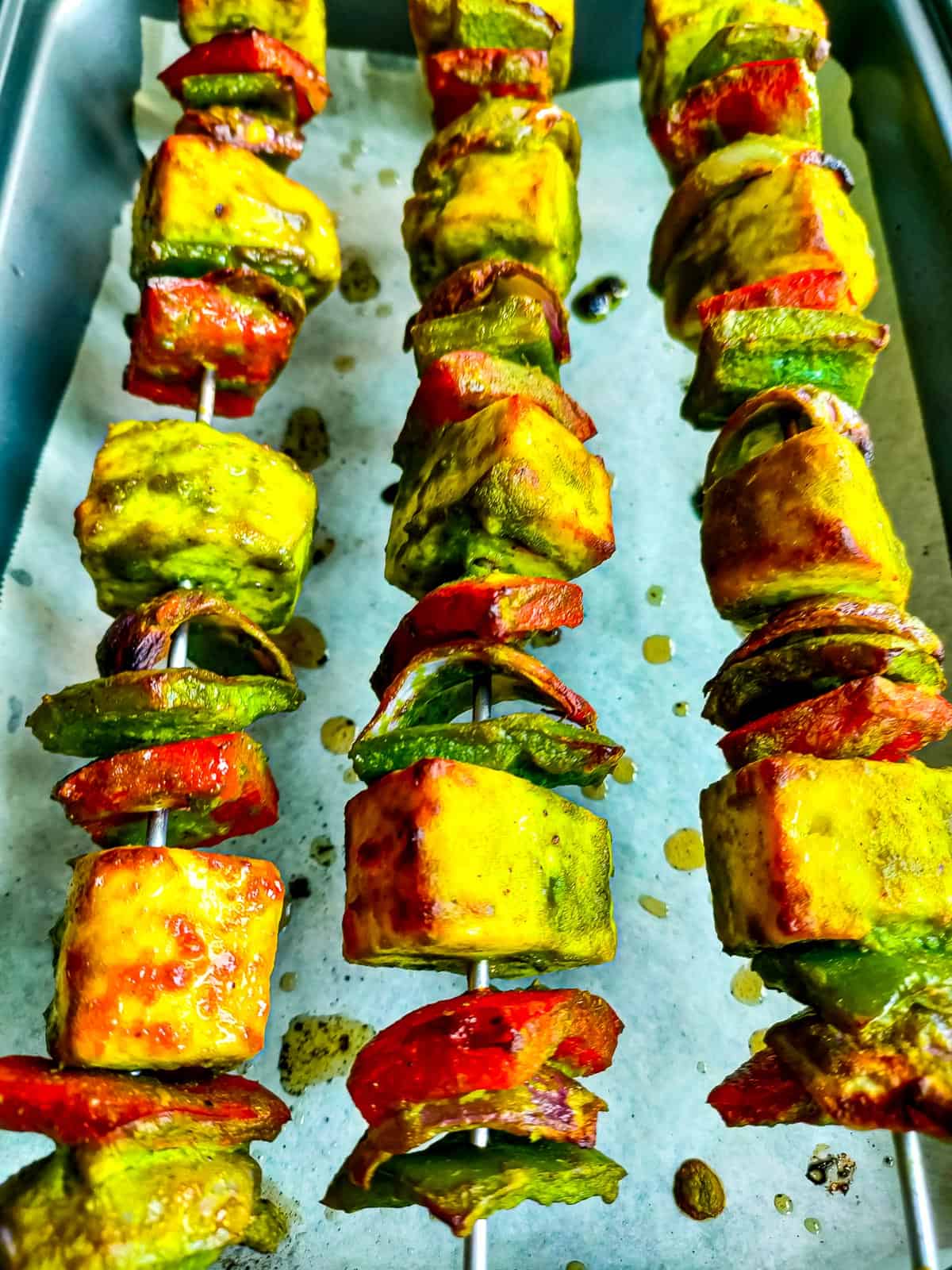 Pudina paneer tikka on skewers on a baking tray lined with parchment paper.