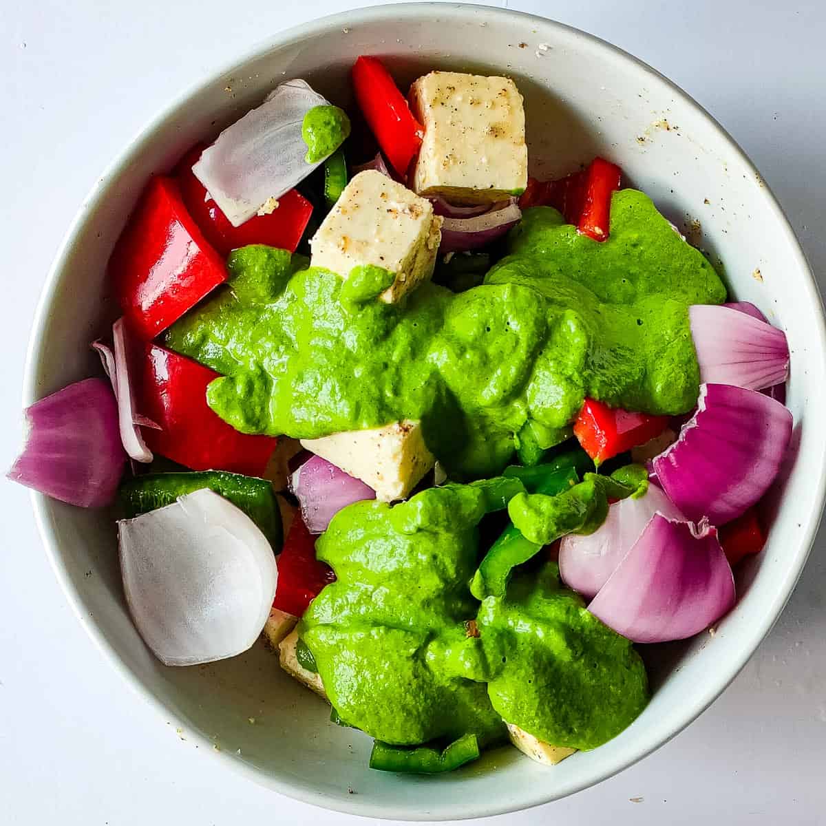 cubed paneer, pepper and onion with pudina marinade in a white bowl.