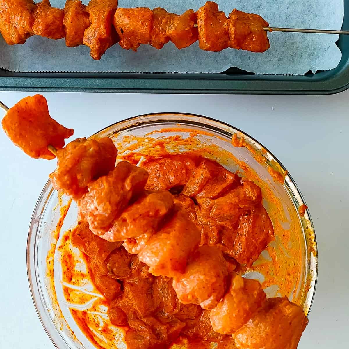 Marinated chicken tikka being threaded on skewers.