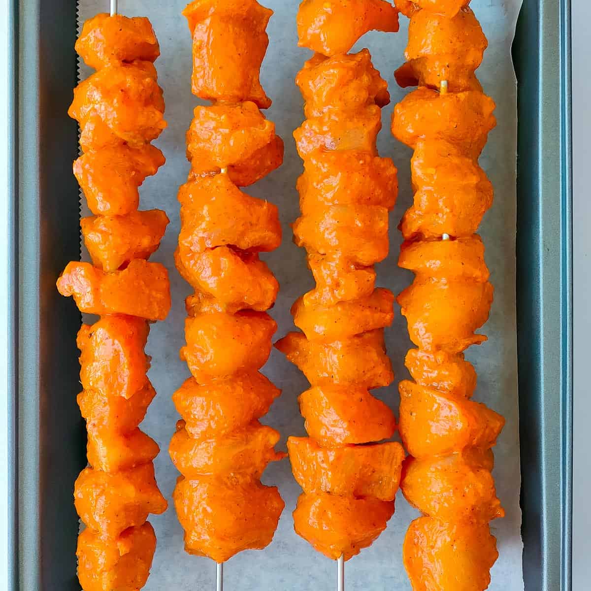 Easy Tandoori Chicken Tikka Marinated tandoori chicken tikka on skewers on a baking pan, ready to be baked.