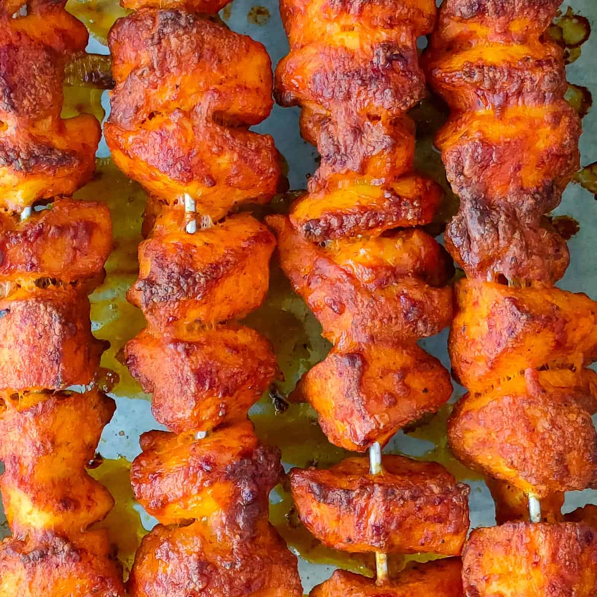 Easy Tandoori Chicken Tikka Tandoori chicken skewers on a baking pan.