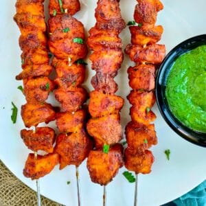 Chicken tandoori skewers served with mint chutney on a white plate.