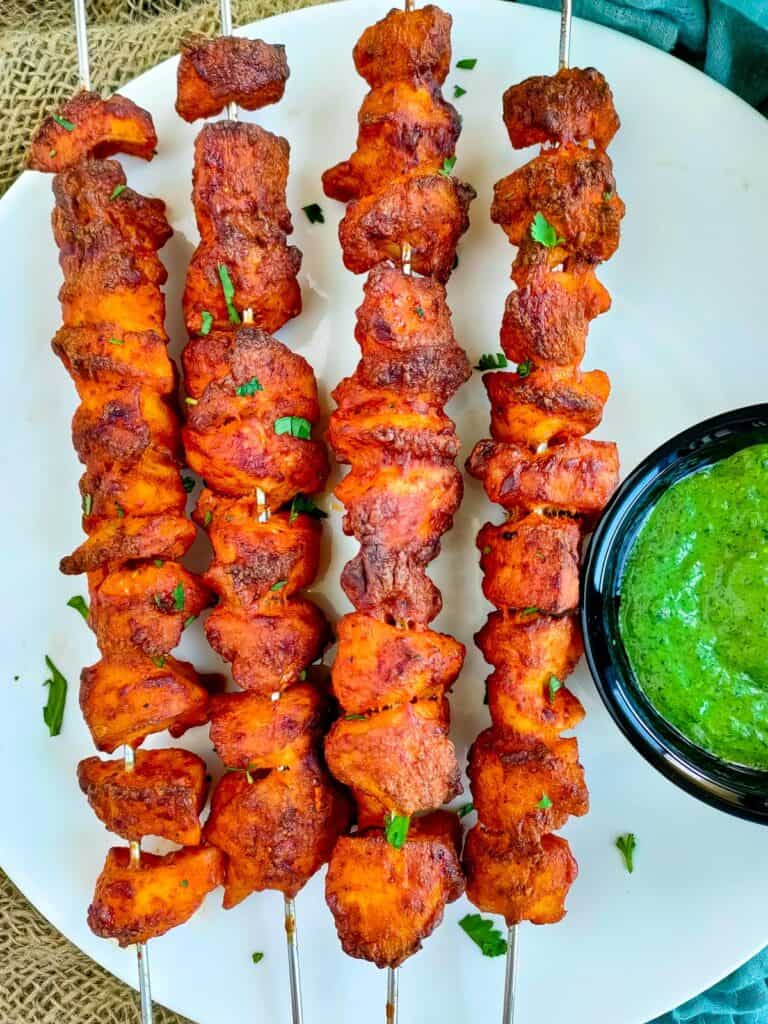 Chicken tandoori skewers served with mint chutney on a white plate.
