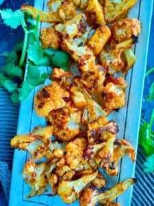 roasted tandoori cauliflower garnished with coriander leaves on a white plate.