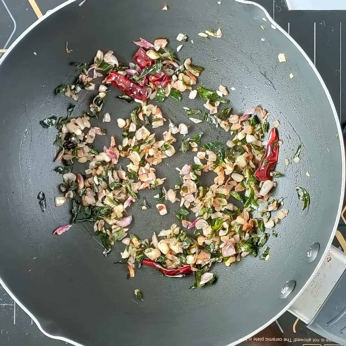 Onions and chillies being roasted in a pan for tempering Kerala chicken curry.