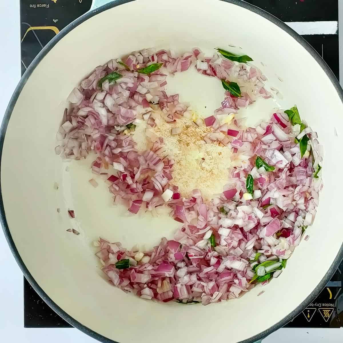 Onions being sauteed in a cooking pot for Kerala chicken curry.