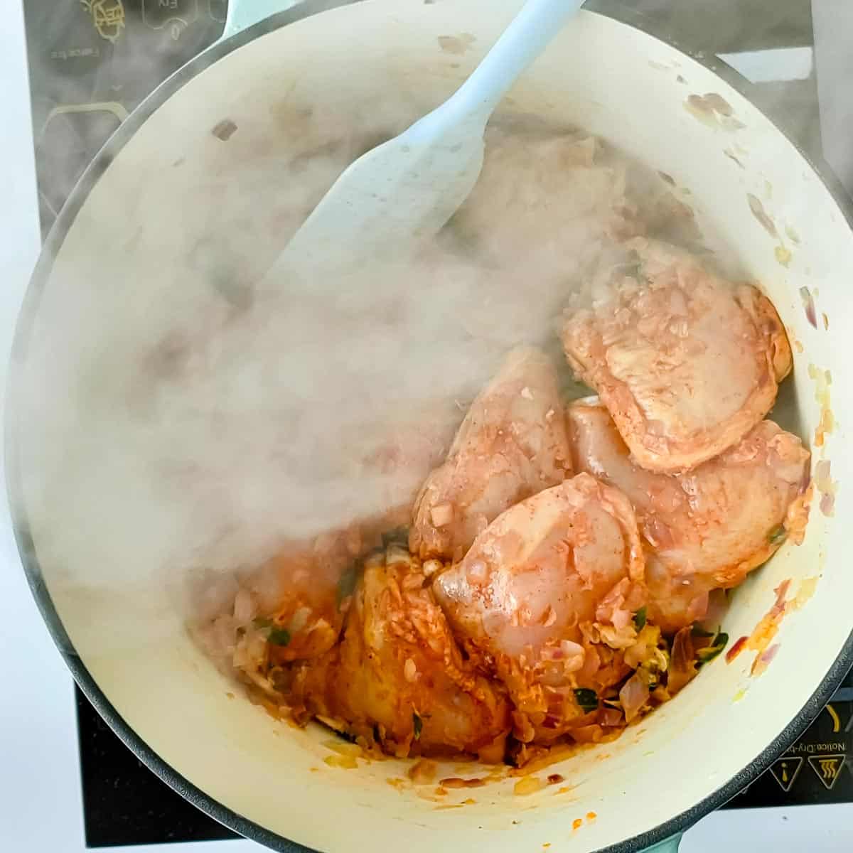 Chicken being sauteed in a cooking pot for Kerala chicken curry.