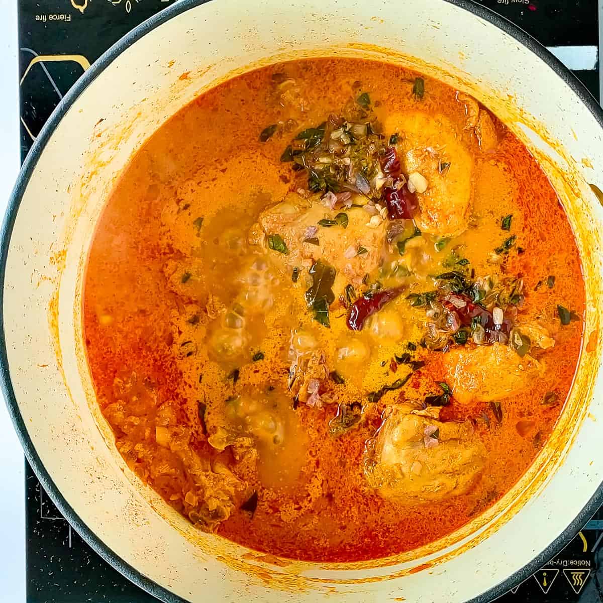 Tempering added to simmering Kerala chicken curry in a cooking pot.