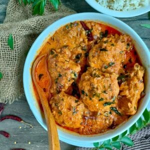 Kerala chicken curry in a white bowl with a spoon in it. and a bowl of rice next to it.