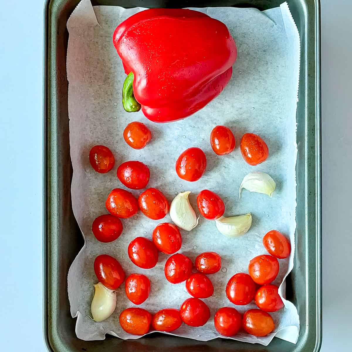 Red bell pepper, cherry tomatoes and garlic ready to be roasted in a pan.