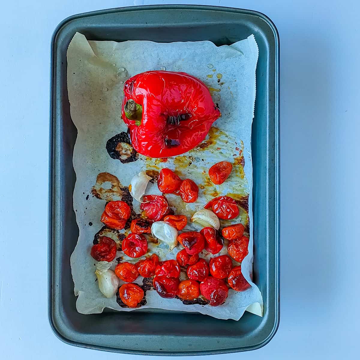 Roasted bell pepper, cherry tomatoes and garlic in a roasting pan.