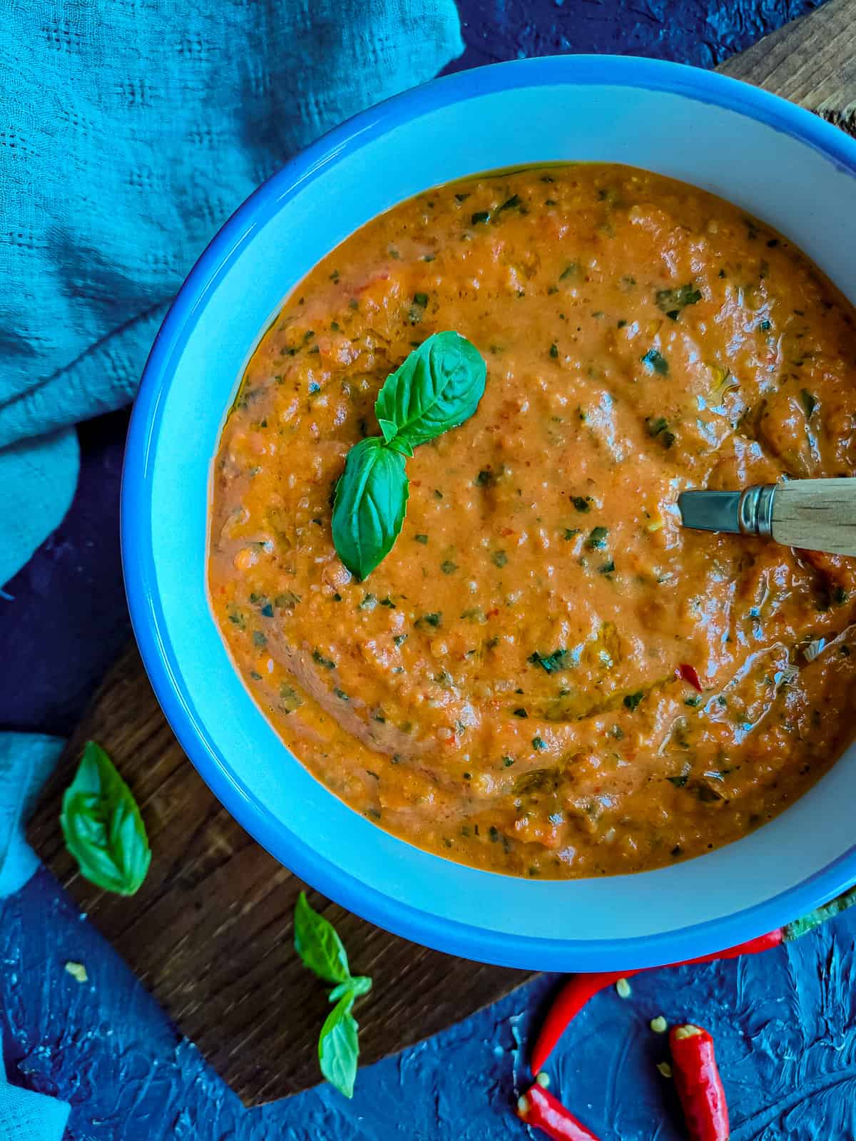 red chilli pesto with almonds in a blue bowl with a spoon in it.