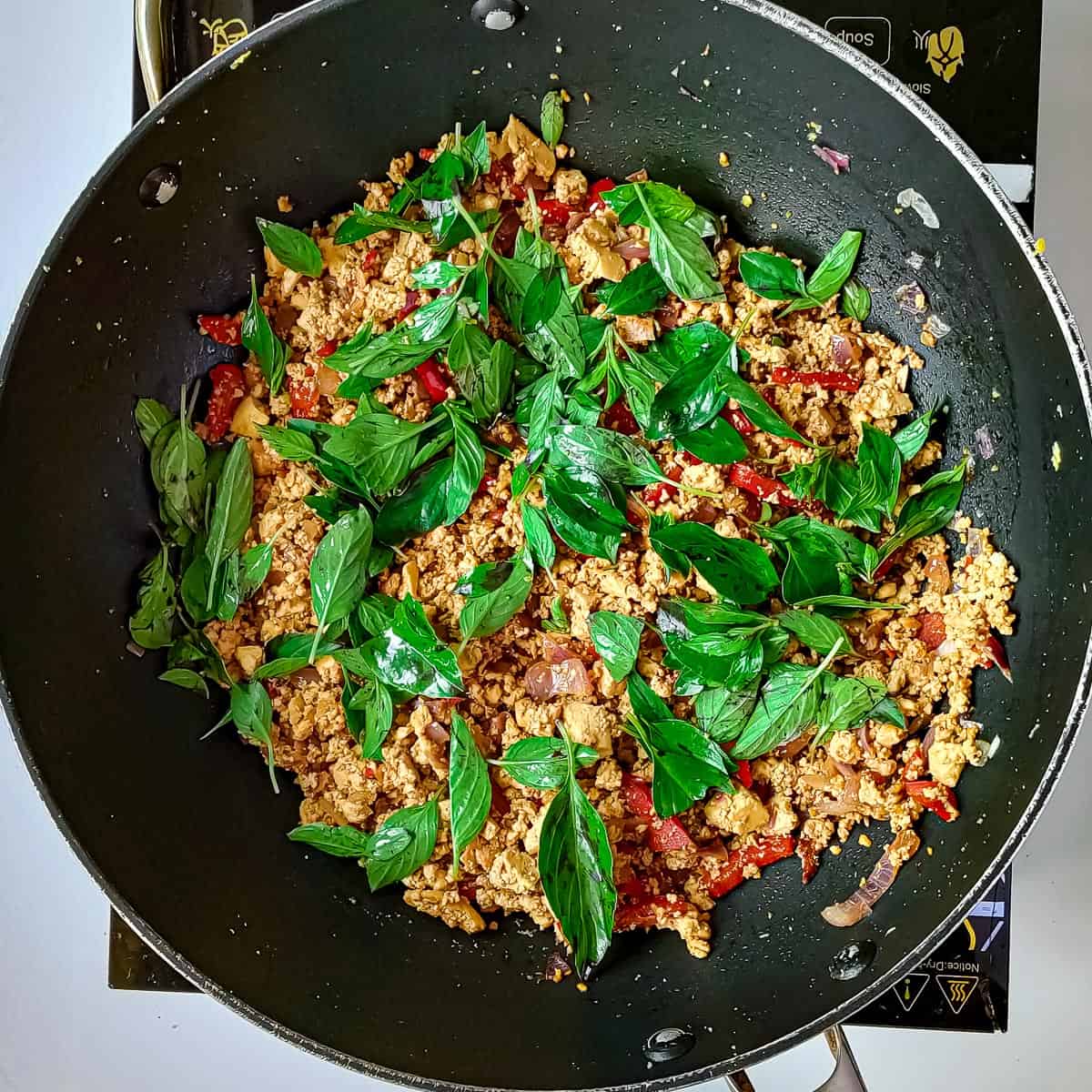 Thai basil added to stir fried tofu in a wok.