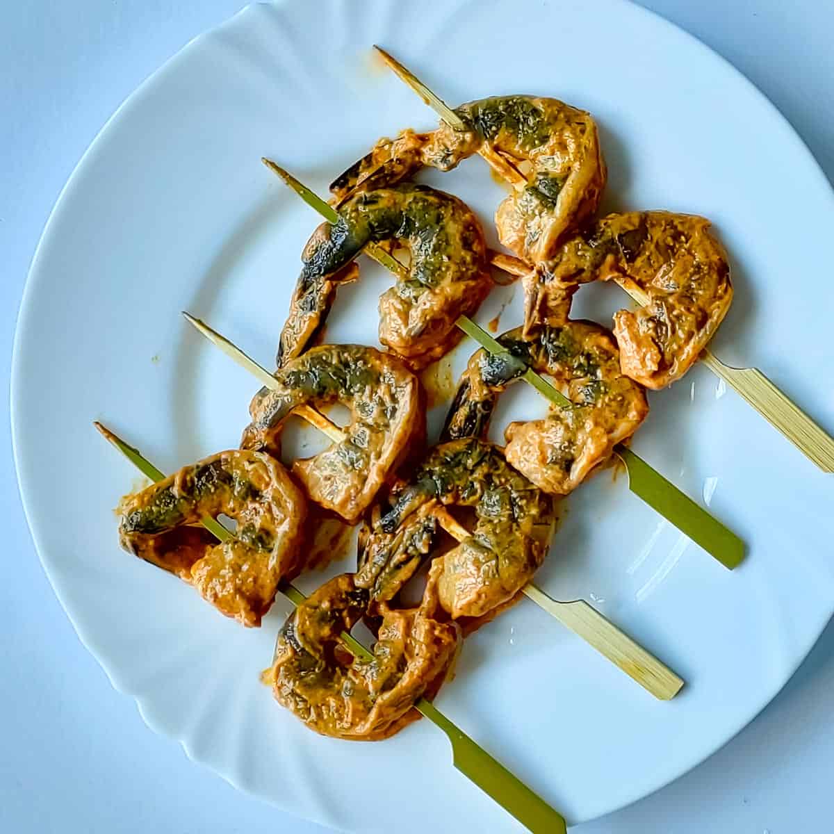 Marinated tandoori king prawns on skewers on a white plate.