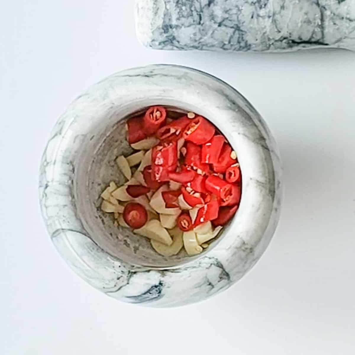 Chopped garlic and chillies in a mortar ready to be crushed.