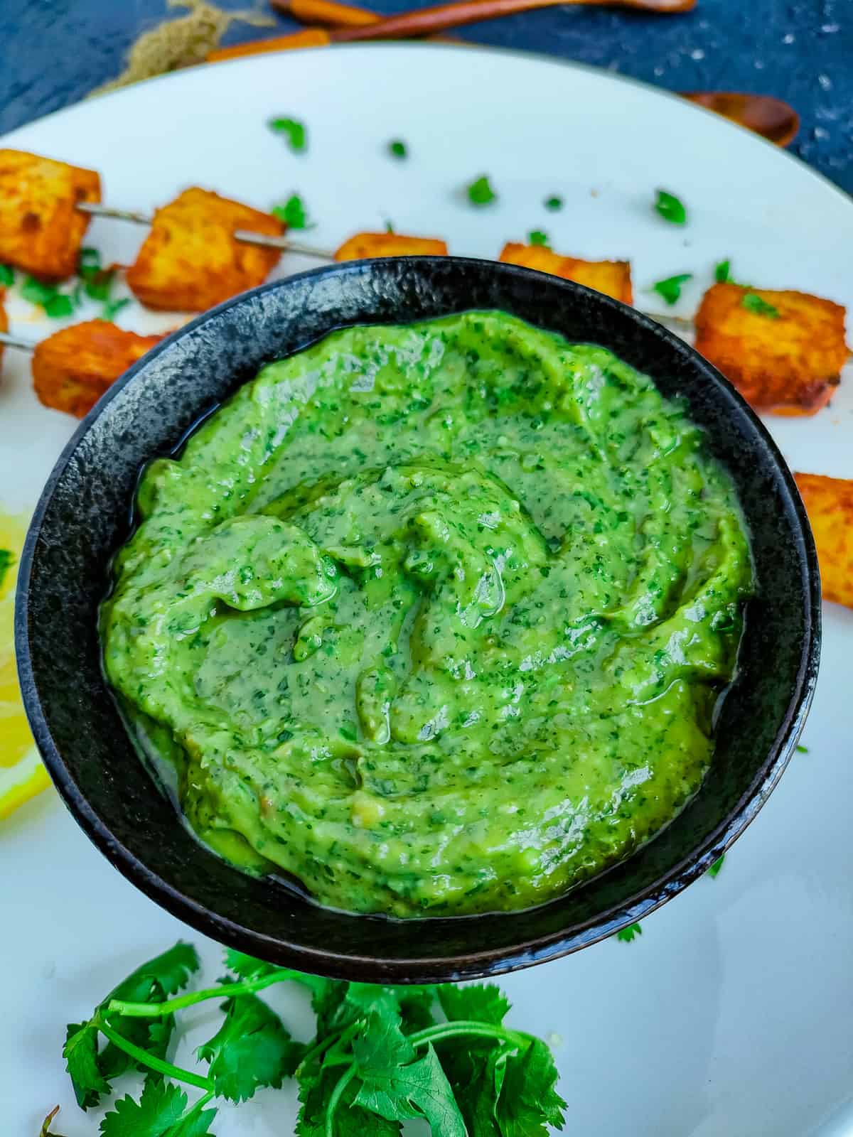 Avocado chutney in a black bowl served with paneer tikka skewers.