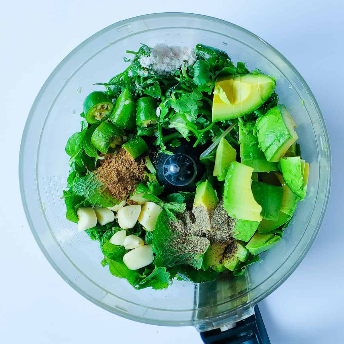 Chopped ingredients for avocado chutney in a food processor jar.