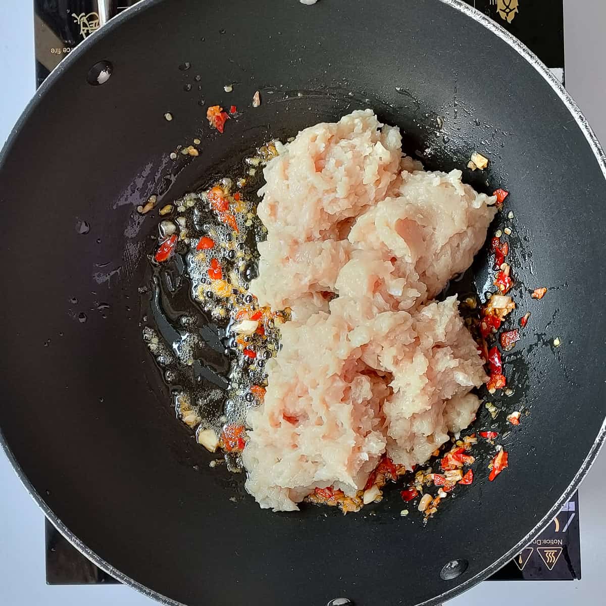 Minced chicken added to chili garlic paste in a wok.