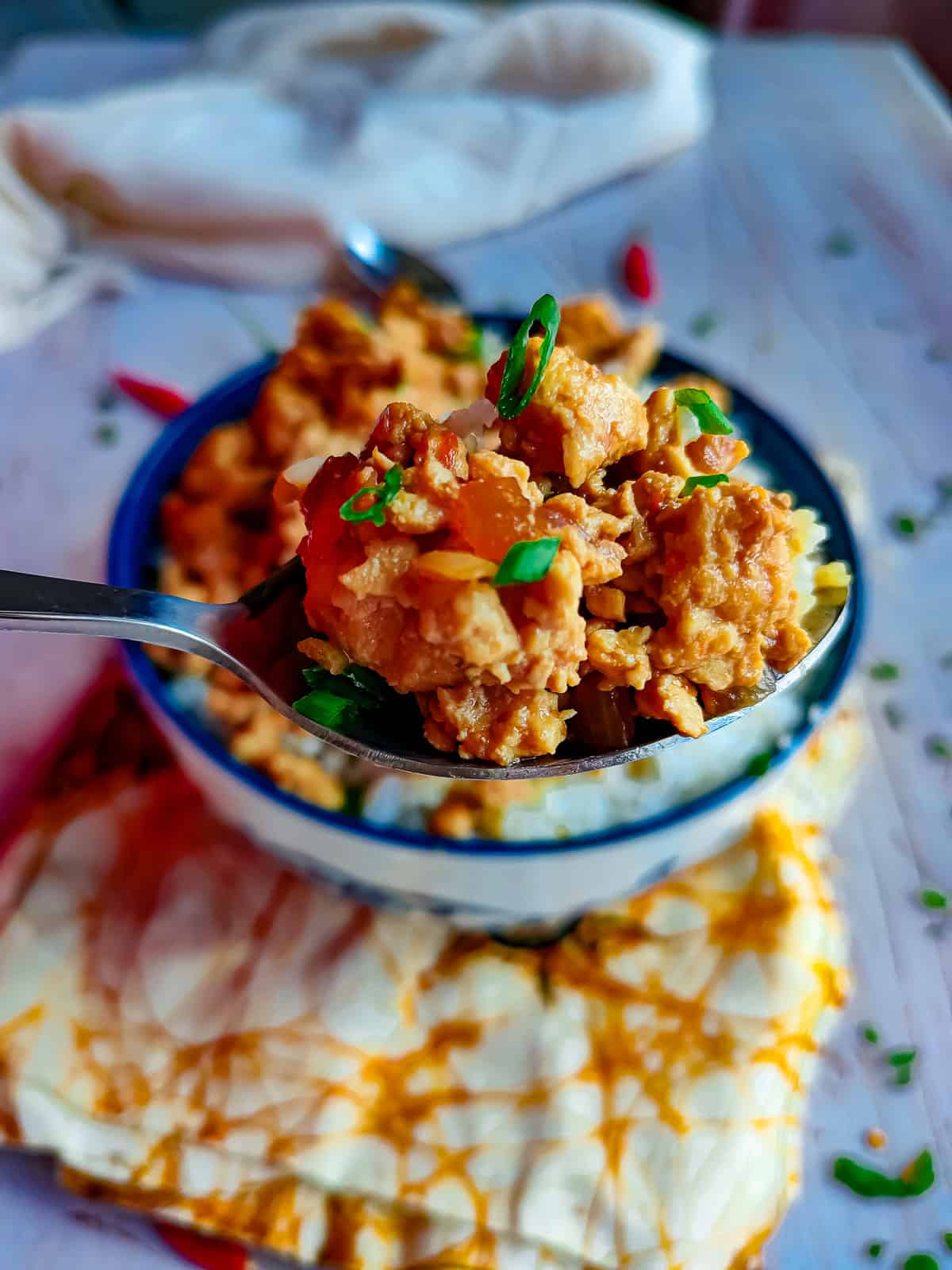 Chicken mince stir fry in a spoon with a bowl of the stir fry with rice in the background.