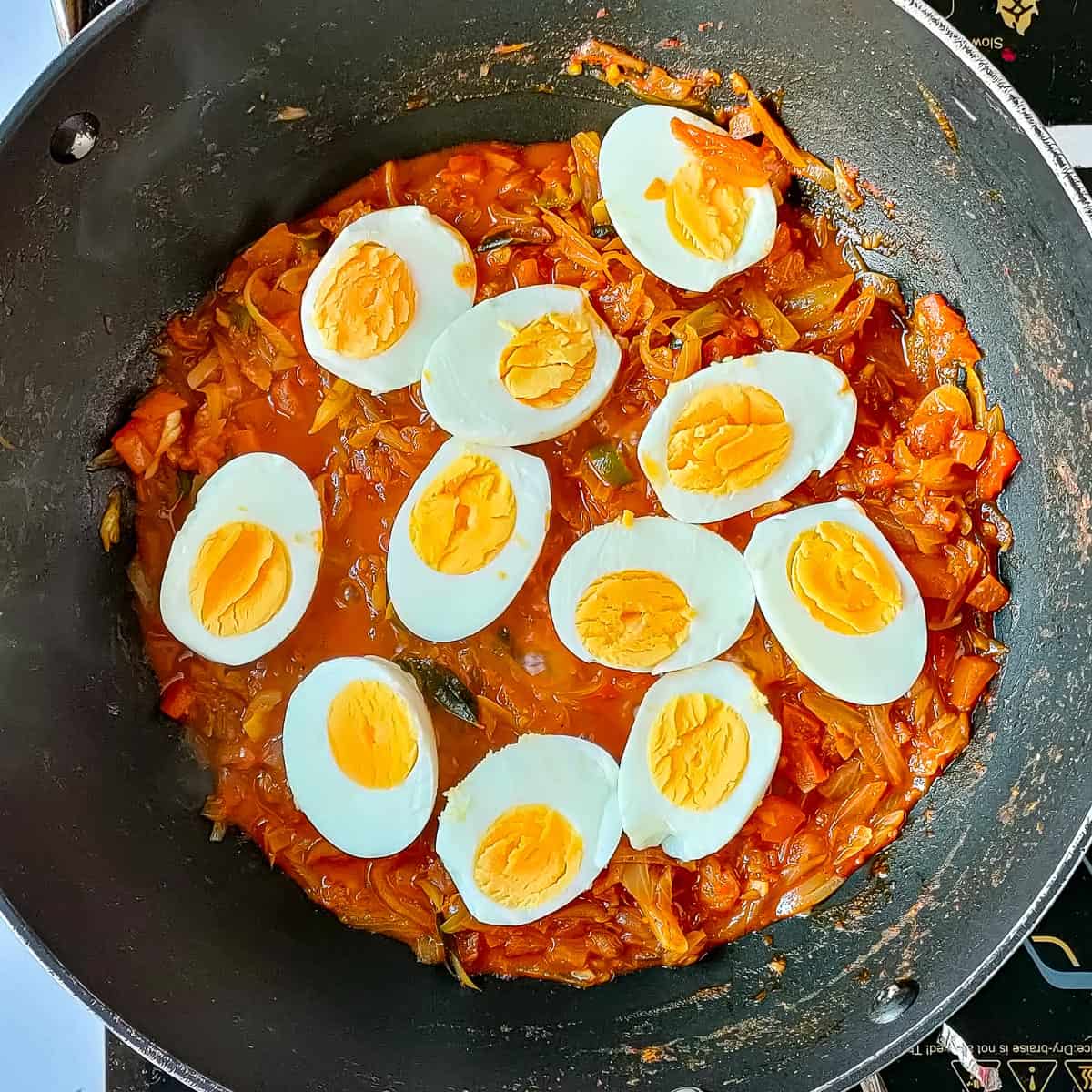Boiled and halved eggs added to the gravy in a wok for Kerala egg roast.