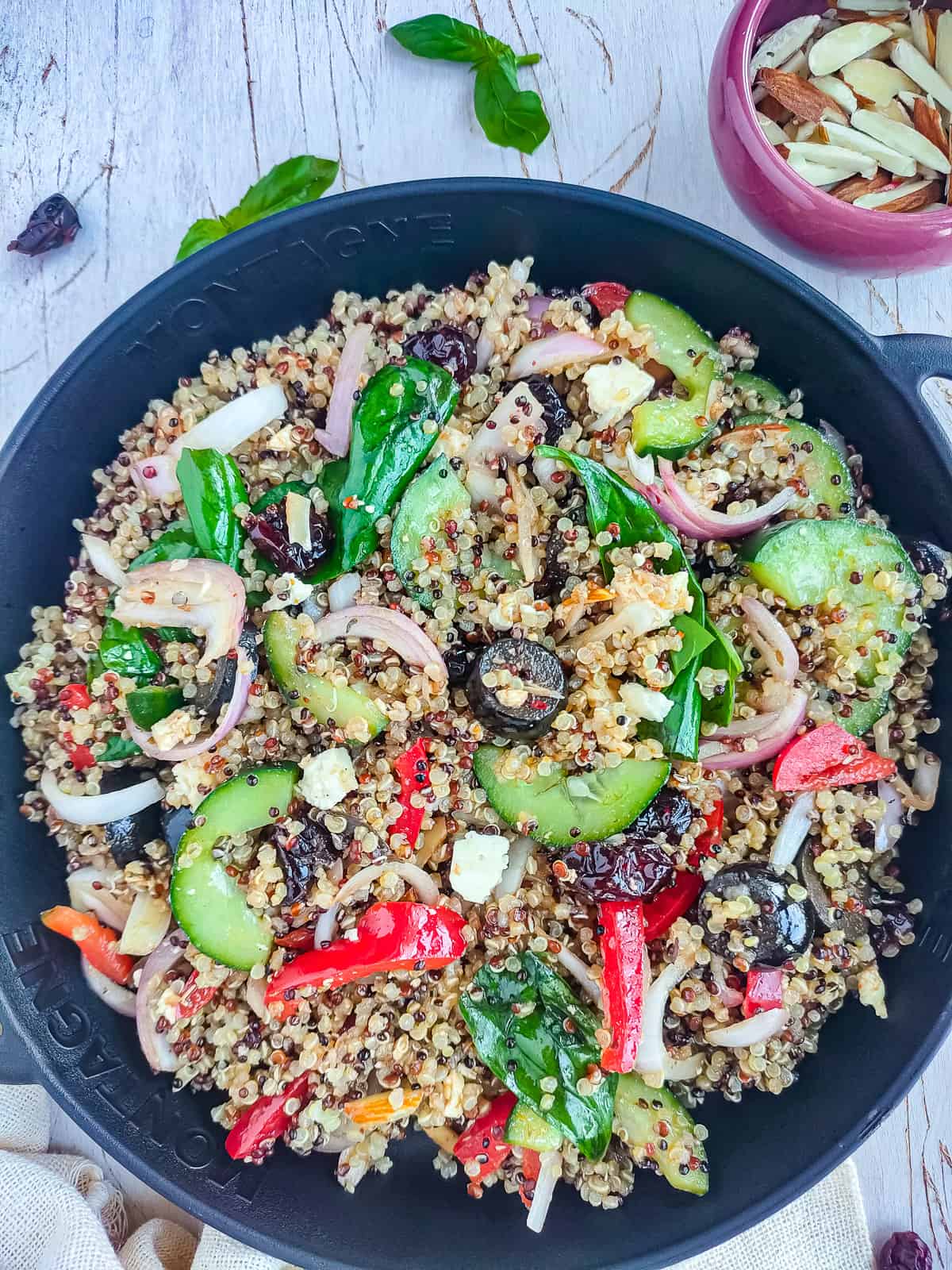 Quinoa salad with balsamic dressing on a black plate and a small bowl of sliced almonds next to it.