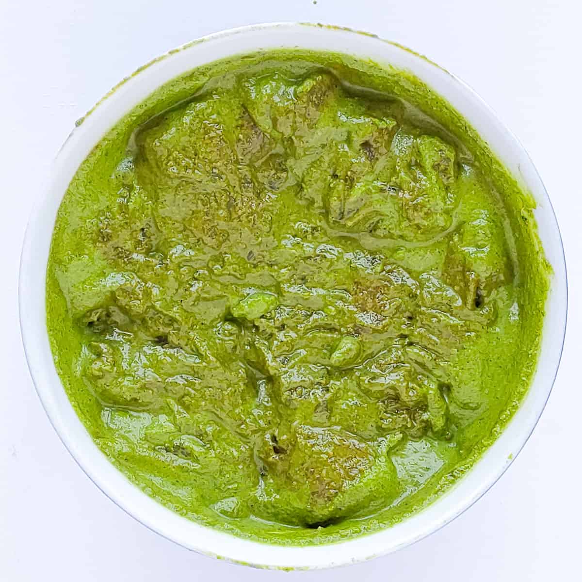 Marinated green chicken kababs in a white bowl.