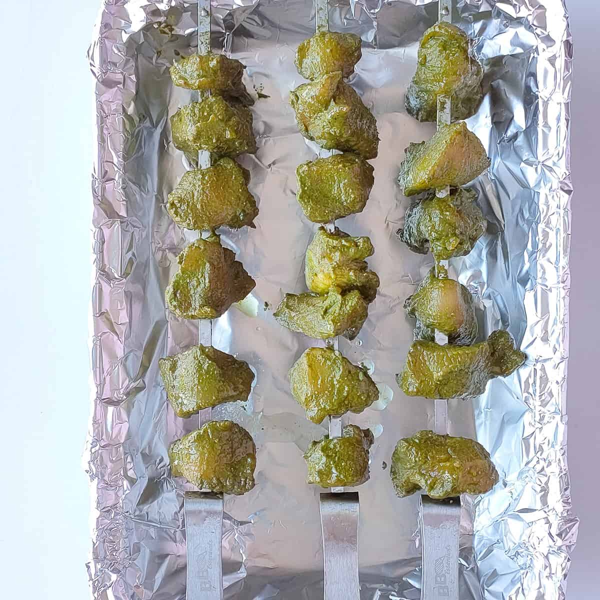 Marinated hariyali chicken tikka on skewers placed on a baking tray lined with foil.