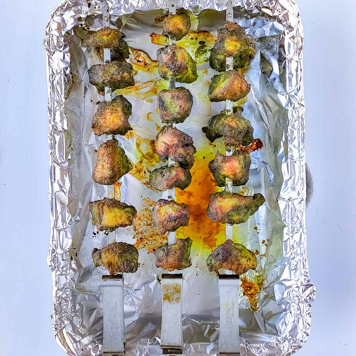 Roasted chicken hariyali tikka on skewers placed on a baking tray lined with foil.