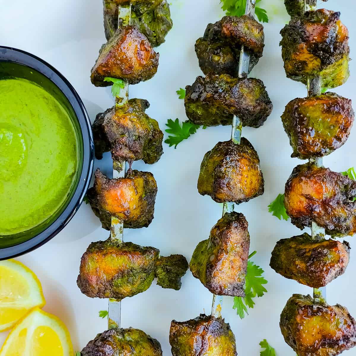 Chicken hariyali kababs on skewers with green chutney on a white plate.