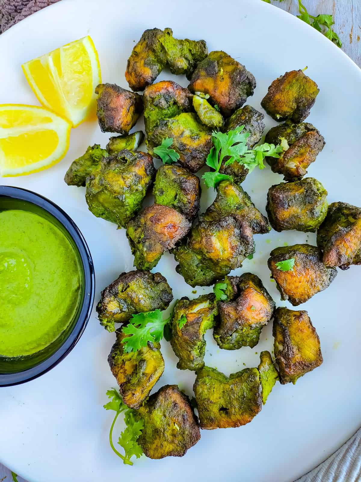 Green chicken kabab with green chutney on a white plate.