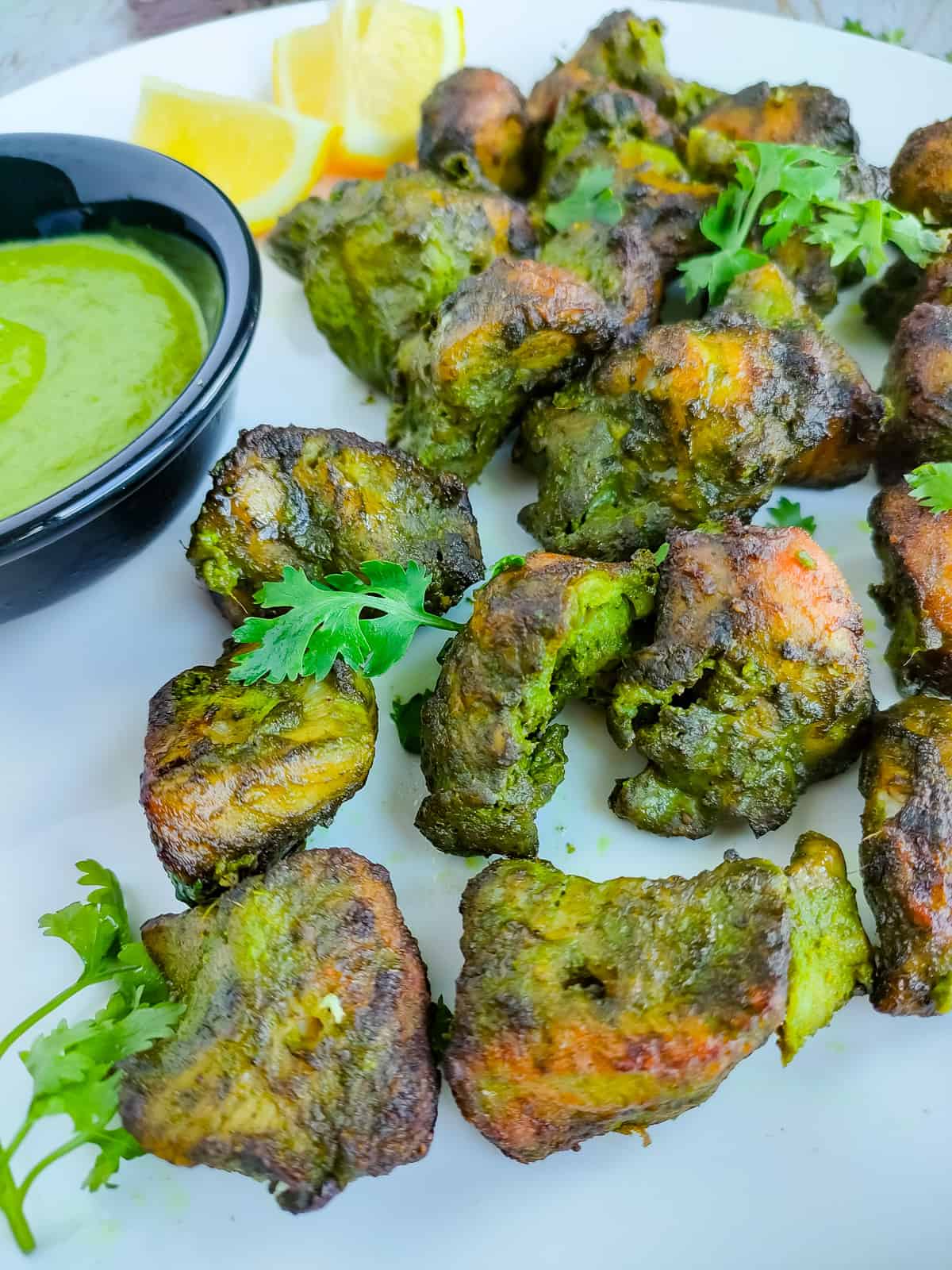 Hariyali chicken kebabs with green chutney on a white plate.