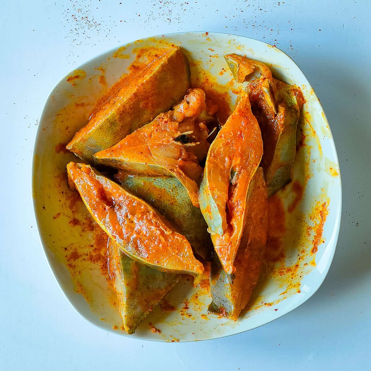 Fish pieces marinated with spices on a white plate.