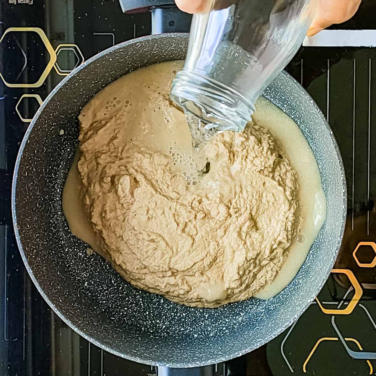 Water being added to coconut paste in a pot.