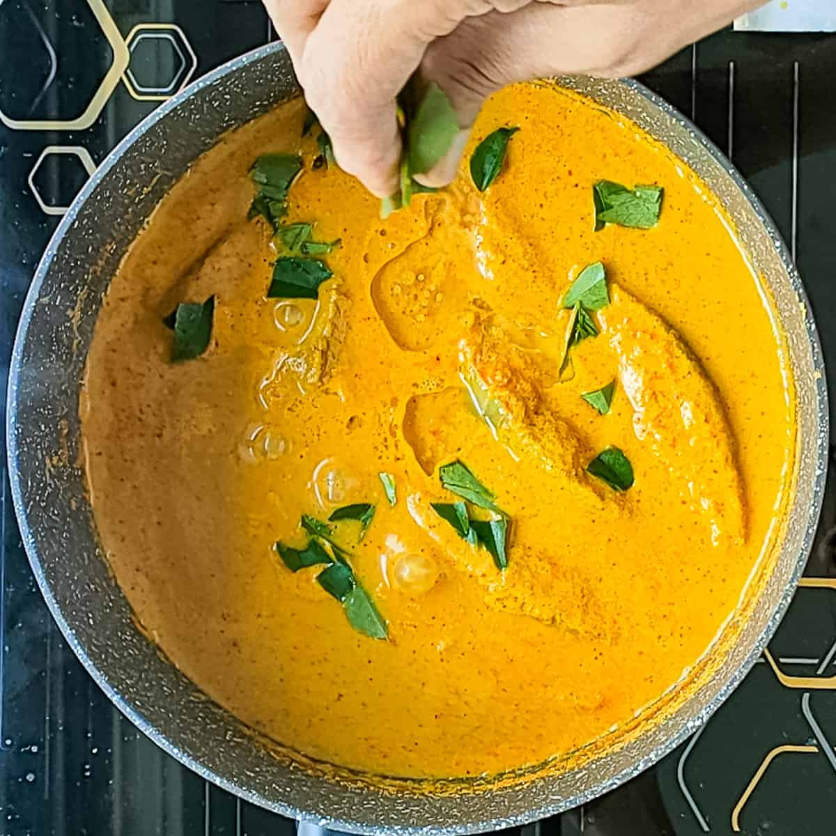 Kerala fish curry being garnished with curry leaves.