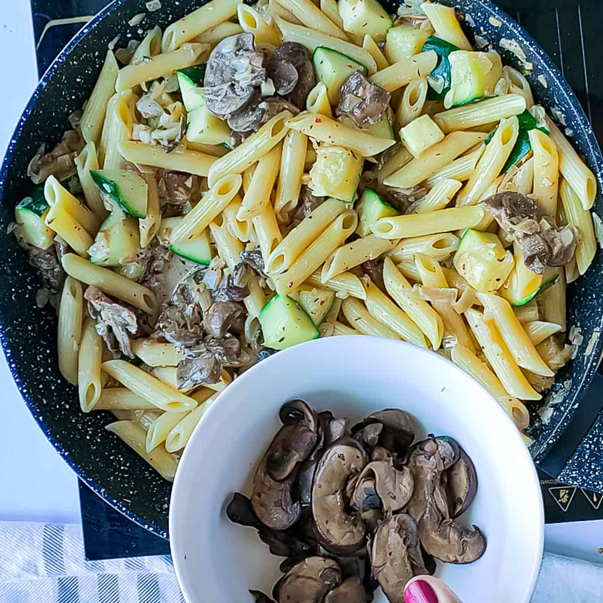 Sauteed mushrooms being added to mushroom and zucchini pasta in a pan.